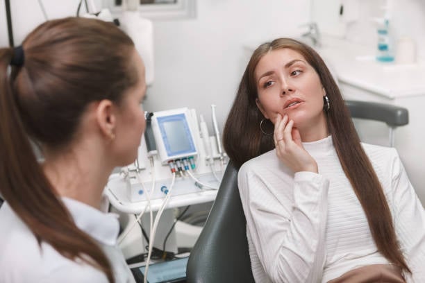 A patient in a dental chair holding her jaw while speaking with a clinician