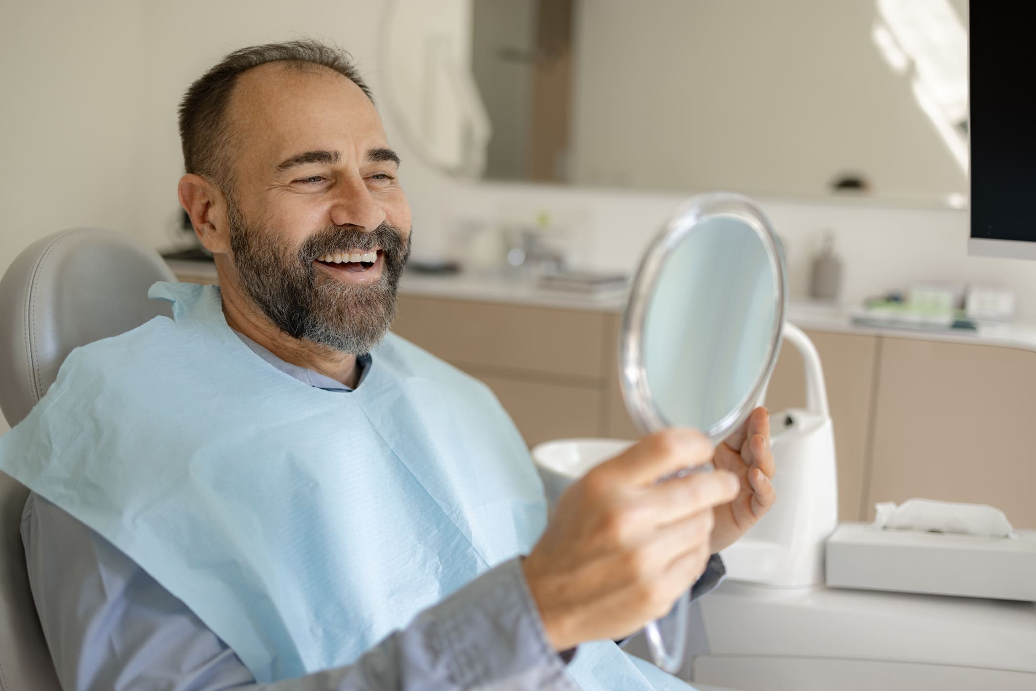 A smiling patient looking in a hand mirror
